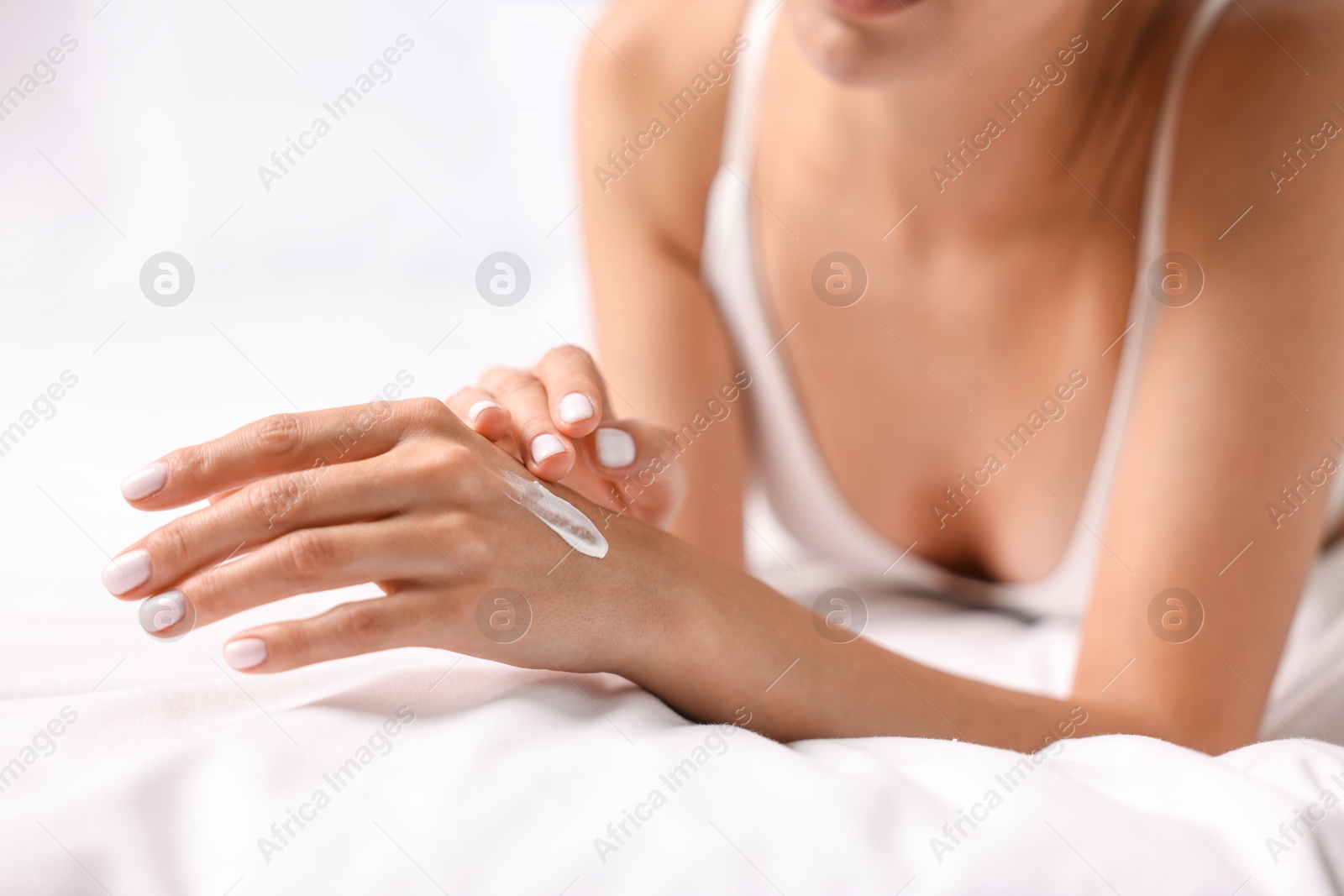 Photo of Woman applying cream onto hand on bed, closeup. Body care