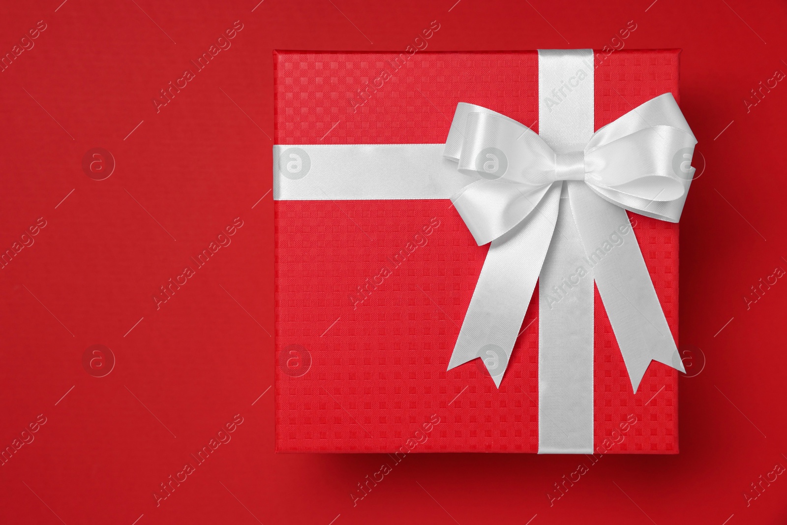 Photo of Gift box with white bow on red background, top view