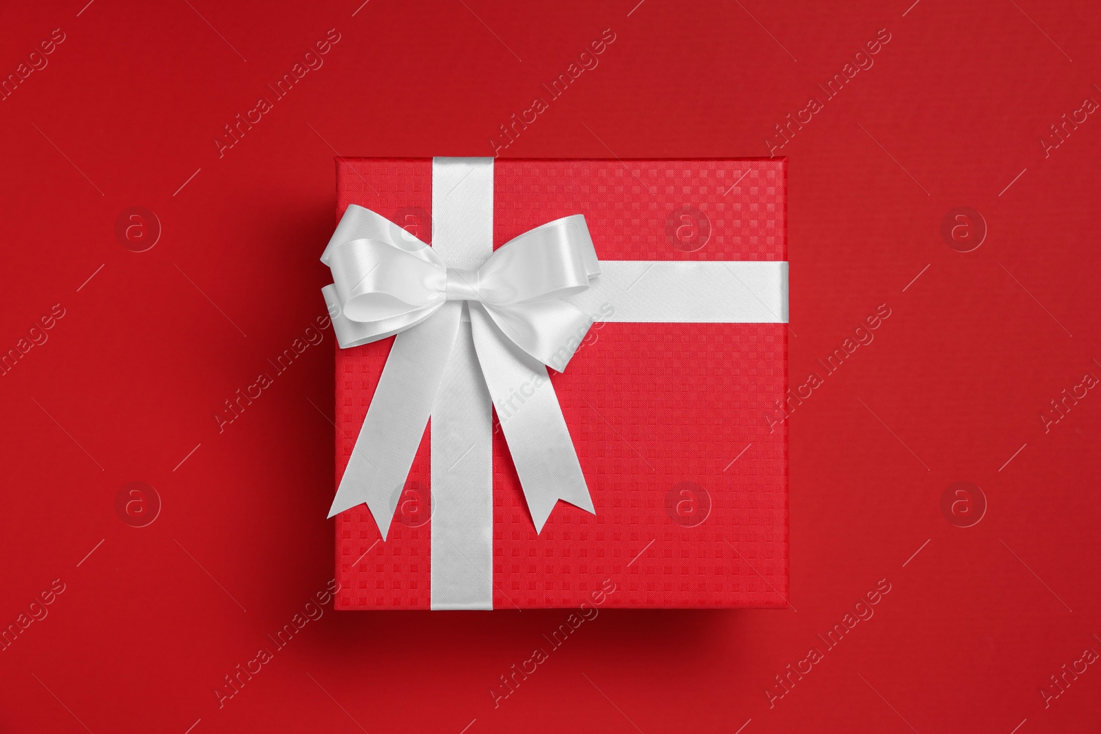 Photo of Gift box with white bow on red background, top view