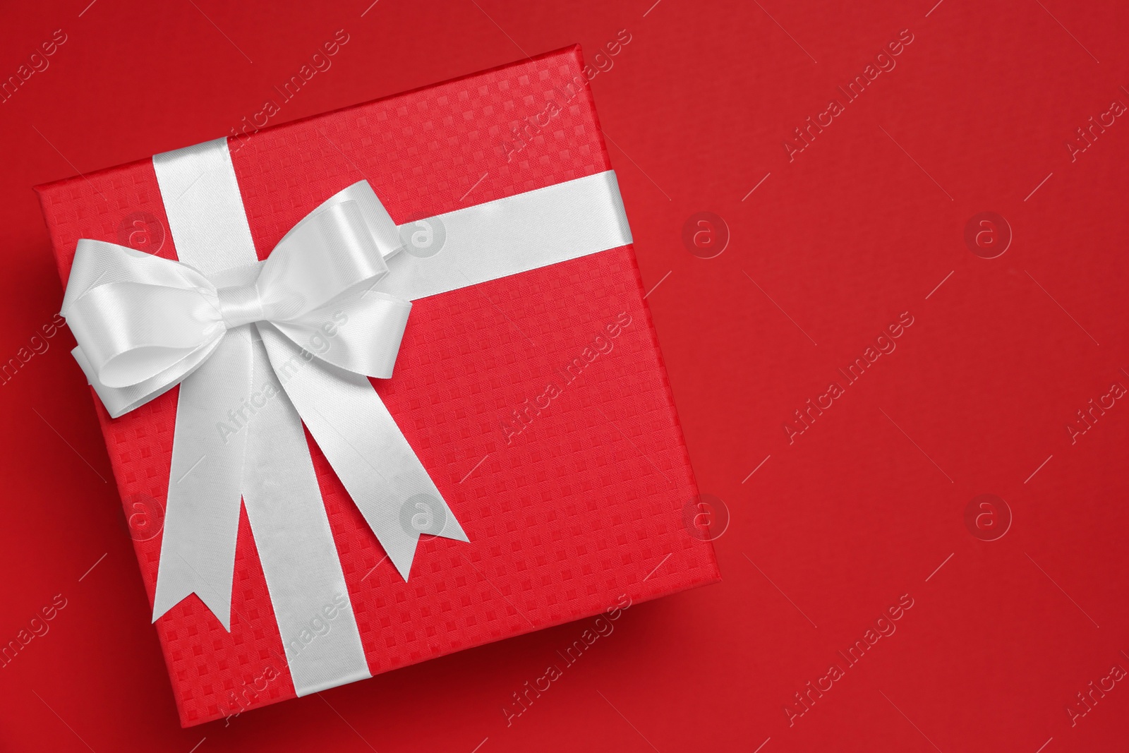 Photo of Gift box with white bow on red background, top view. Space for text