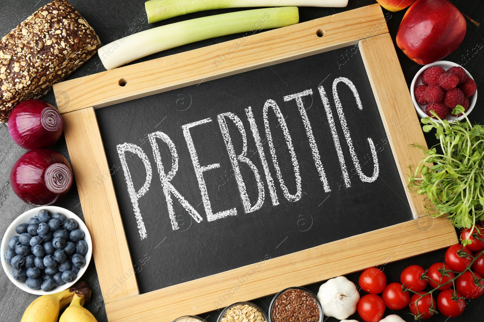 Photo of Chalkboard with word Prebiotic and different fresh products on black table, flat lay