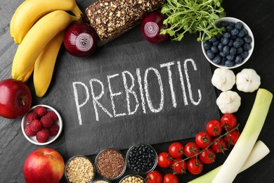 Photo of Slate board with word Prebiotic and different fresh products on black table, flat lay