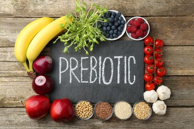 Photo of Slate board with word Prebiotic and different products on wooden table, flat lay