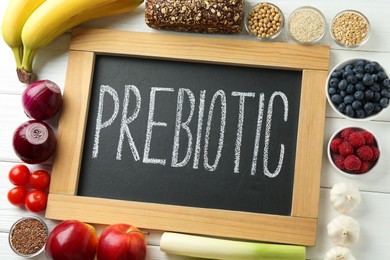 Photo of Chalkboard with word Prebiotic and different products on white wooden table, flat lay