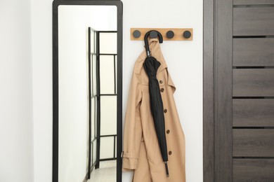 Photo of Black umbrella, coat, rack and mirror in hallway