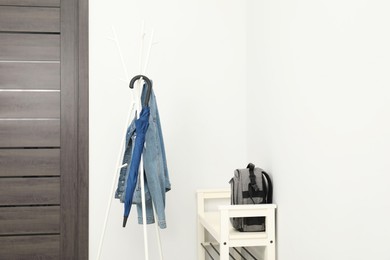 Blue umbrella and denim jacket on clothing rack near shoe storage bench with backpack in hallway