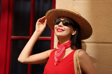 Smiling young woman in stylish hat and sunglasses near building outdoors