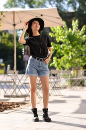 Beautiful young woman in stylish black hat on city street