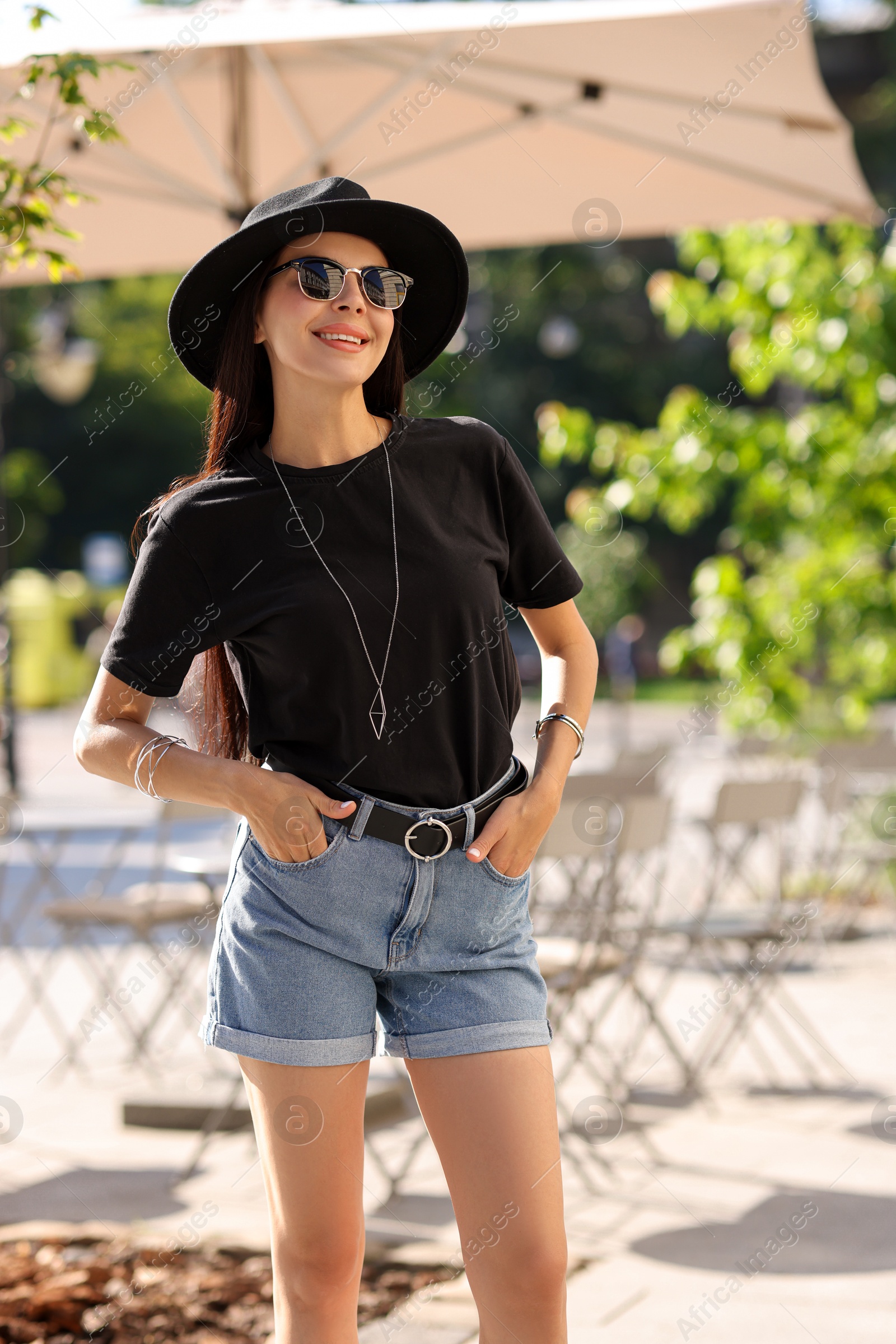 Photo of Smiling woman in stylish black hat and sunglasses on city street