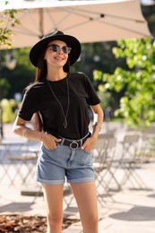 Photo of Smiling woman in stylish black hat and sunglasses on city street