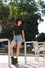 Photo of Young woman in stylish black hat and sunglasses on city street