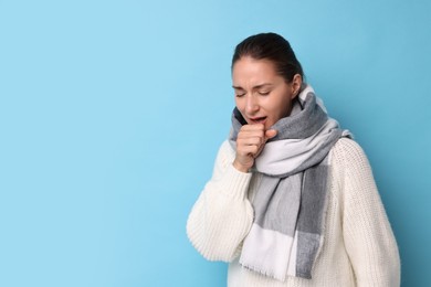 Sick woman coughing on light blue background, space for text. Cold symptoms