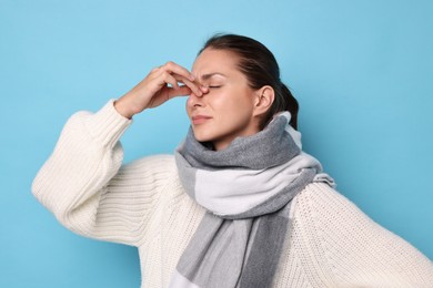 Sick woman suffering from cold symptoms on light blue background