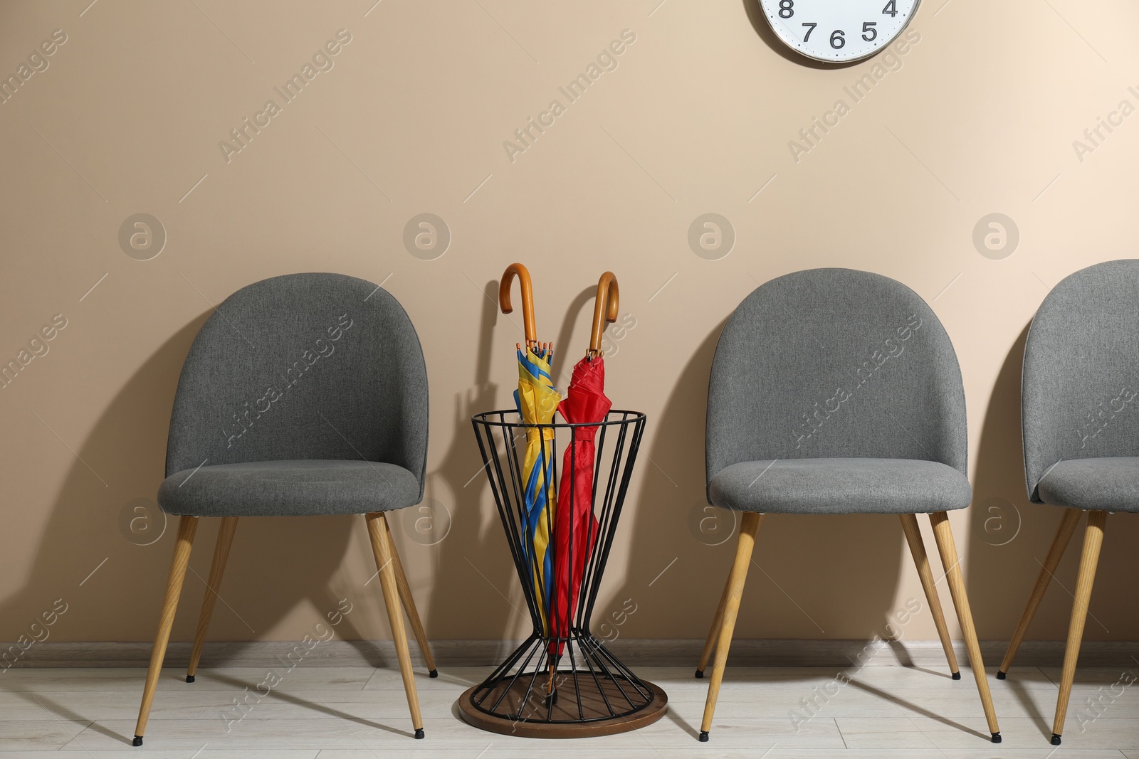 Photo of Holder with bright umbrellas among chairs near beige wall