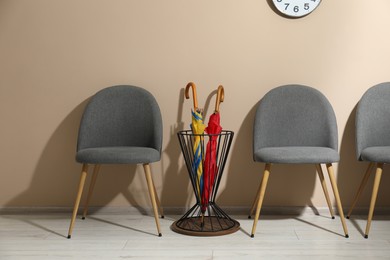 Photo of Holder with bright umbrellas among chairs near beige wall