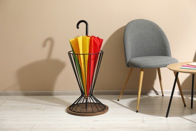 Photo of Bright umbrella in holder, chair and coffee table near beige wall. Space for text