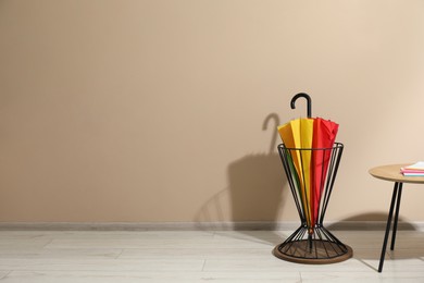 Photo of Bright umbrella in holder and coffee table near beige wall. Space for text