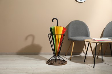 Photo of Bright umbrella in holder, coffee table and chairs near beige wall. Space for text