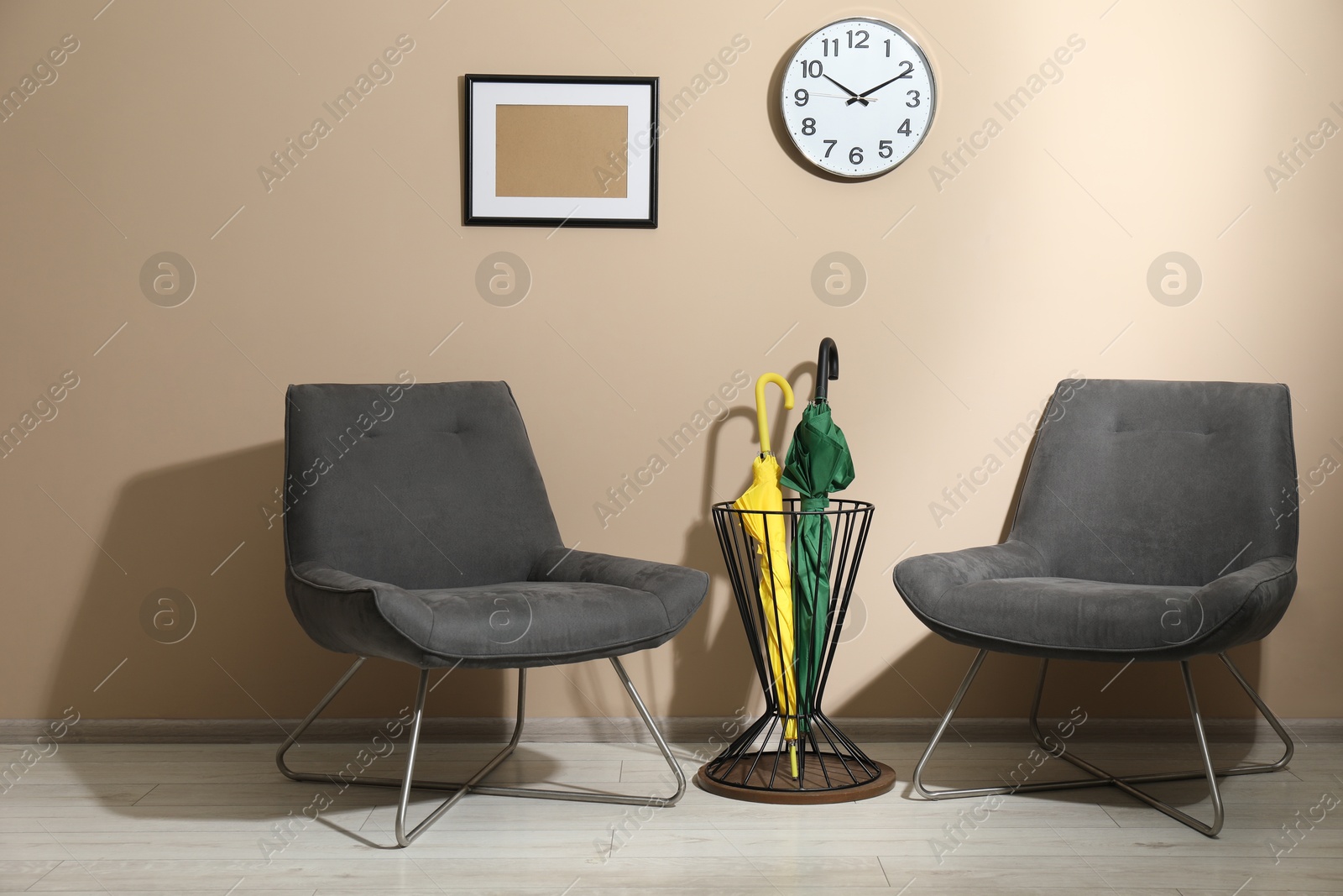 Photo of Bright umbrellas in holder and armchairs near beige wall