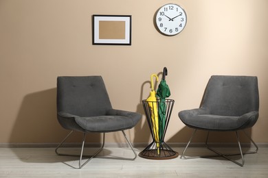 Bright umbrellas in holder and armchairs near beige wall