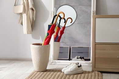 Holder with bright umbrellas, mirror and cabinets in hallway