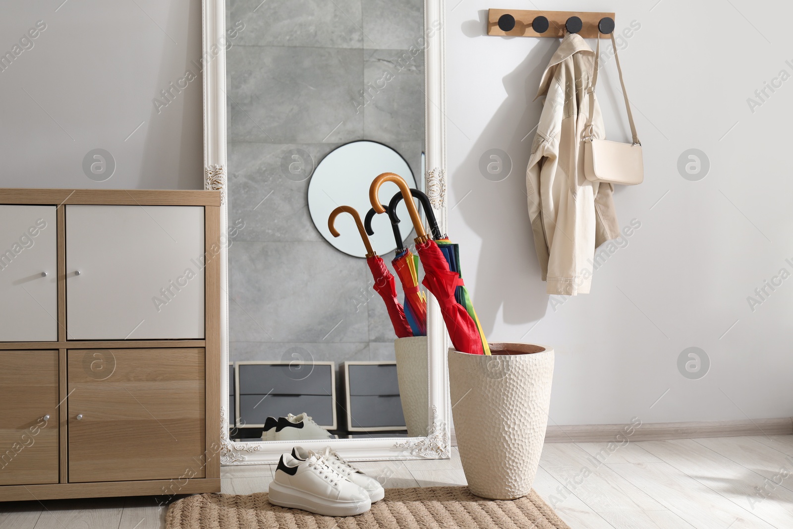 Photo of Holder with bright umbrellas, mirror and cabinets in hallway