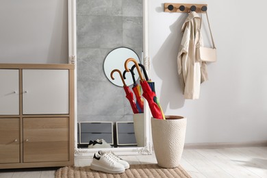 Holder with bright umbrellas, mirror and cabinets in hallway