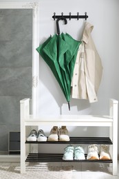 Photo of Green umbrella and jacket on hanger near mirror over shoe storage bench indoors