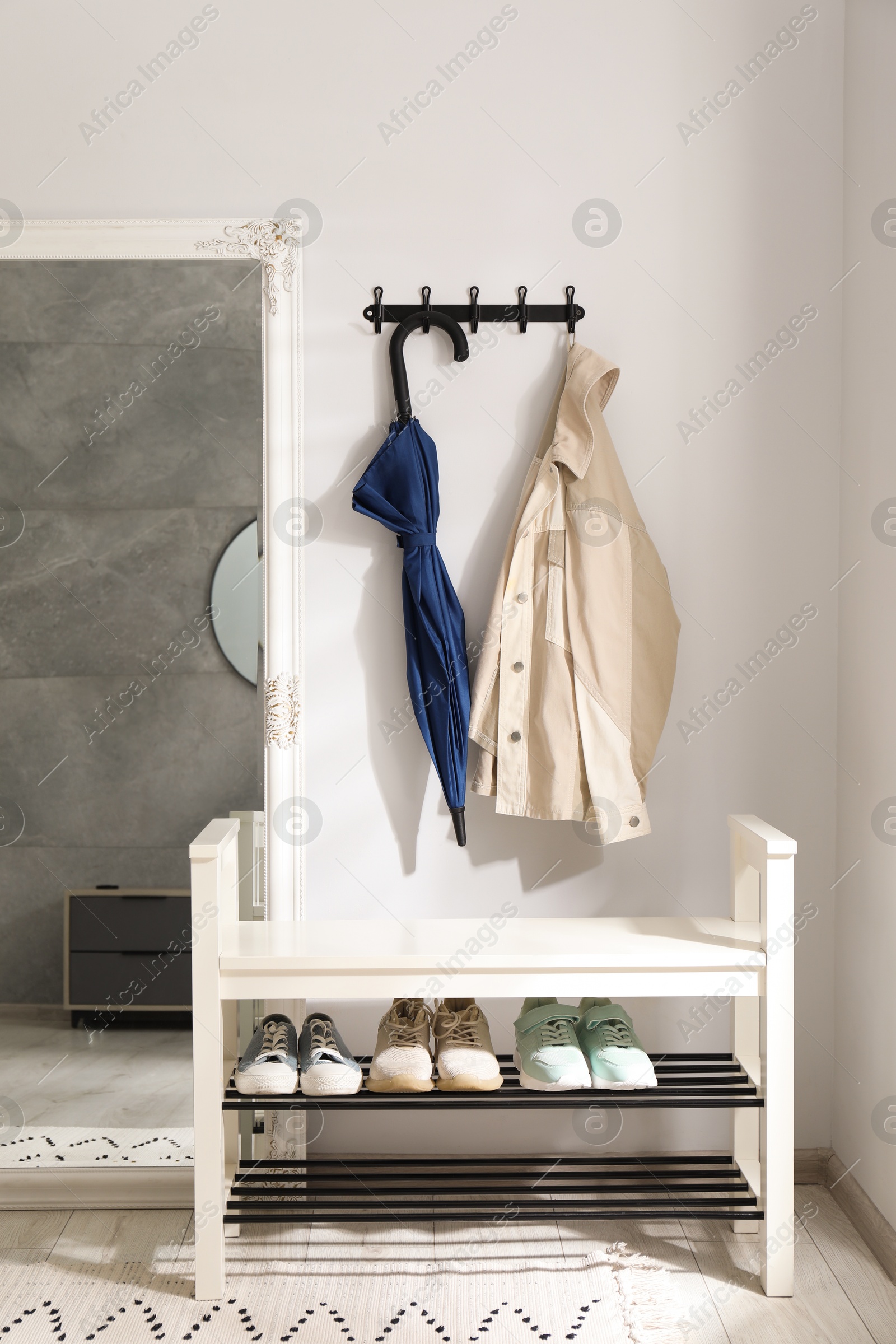 Photo of Blue umbrella and jacket on hanger near mirror over shoe storage bench indoors