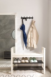 Photo of Blue umbrella and jacket on hanger near mirror over shoe storage bench indoors