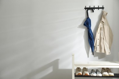 Photo of Blue umbrella and jacket on hanger over shoe storage bench near white wall. Space for text