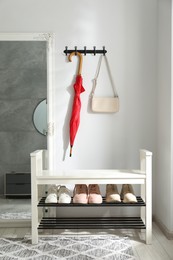 Photo of Red umbrella and bag on hanger near mirror over shoe storage bench indoors