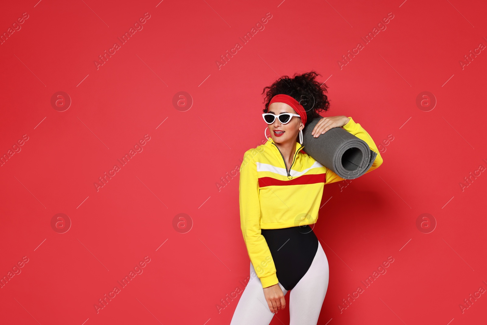 Photo of Aerobics. Woman in sportswear holding fitness mat on red background, space for text