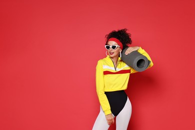 Photo of Aerobics. Woman in sportswear holding fitness mat on red background, space for text