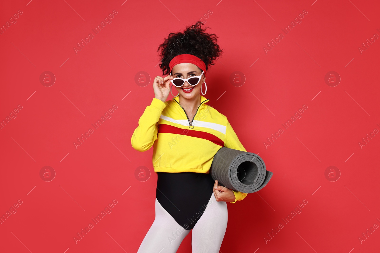 Photo of Aerobics. Woman in sportswear holding fitness mat on red background