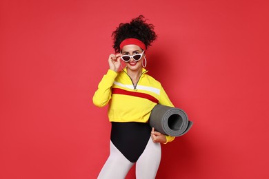 Photo of Aerobics. Woman in sportswear holding fitness mat on red background