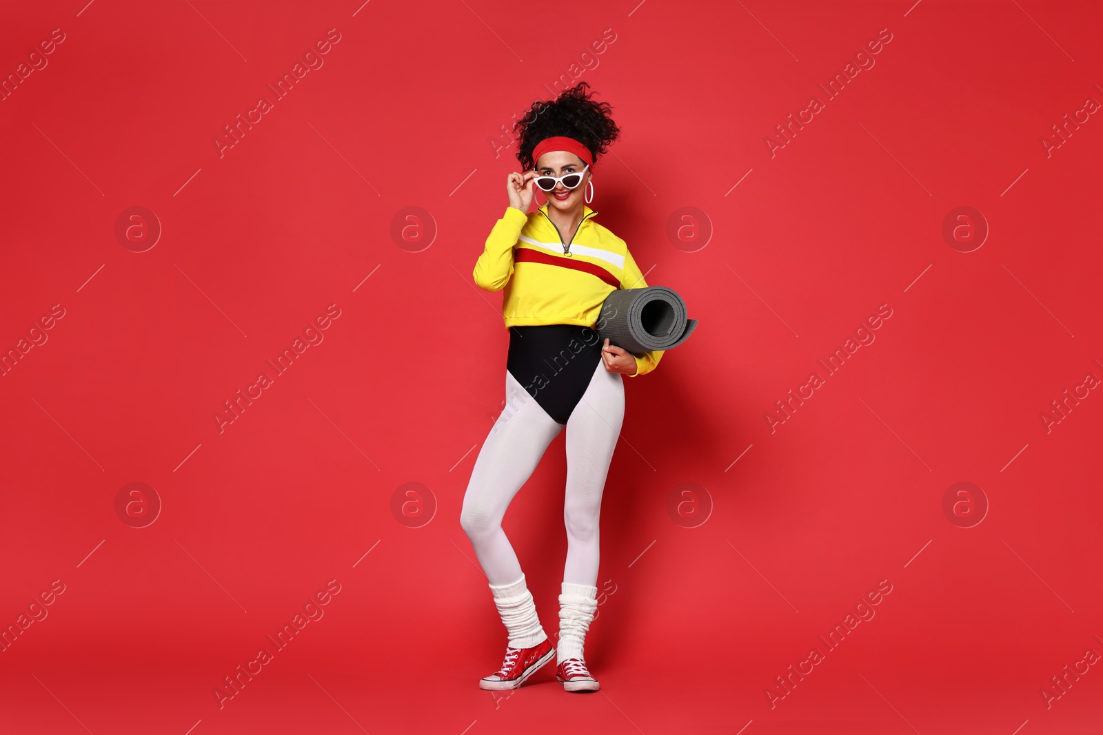 Photo of Aerobics. Woman in sportswear holding fitness mat on red background