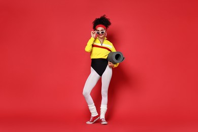 Aerobics. Woman in sportswear holding fitness mat on red background