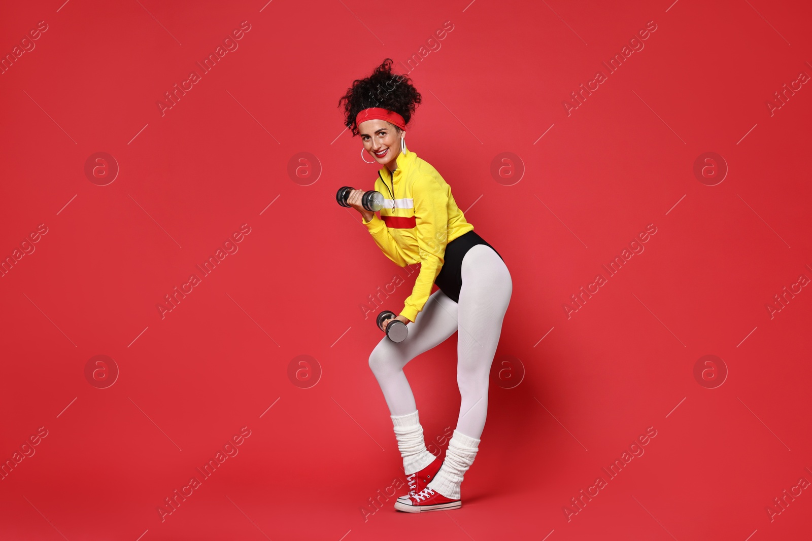 Photo of Woman doing aerobic exercise with dumbbells on red background