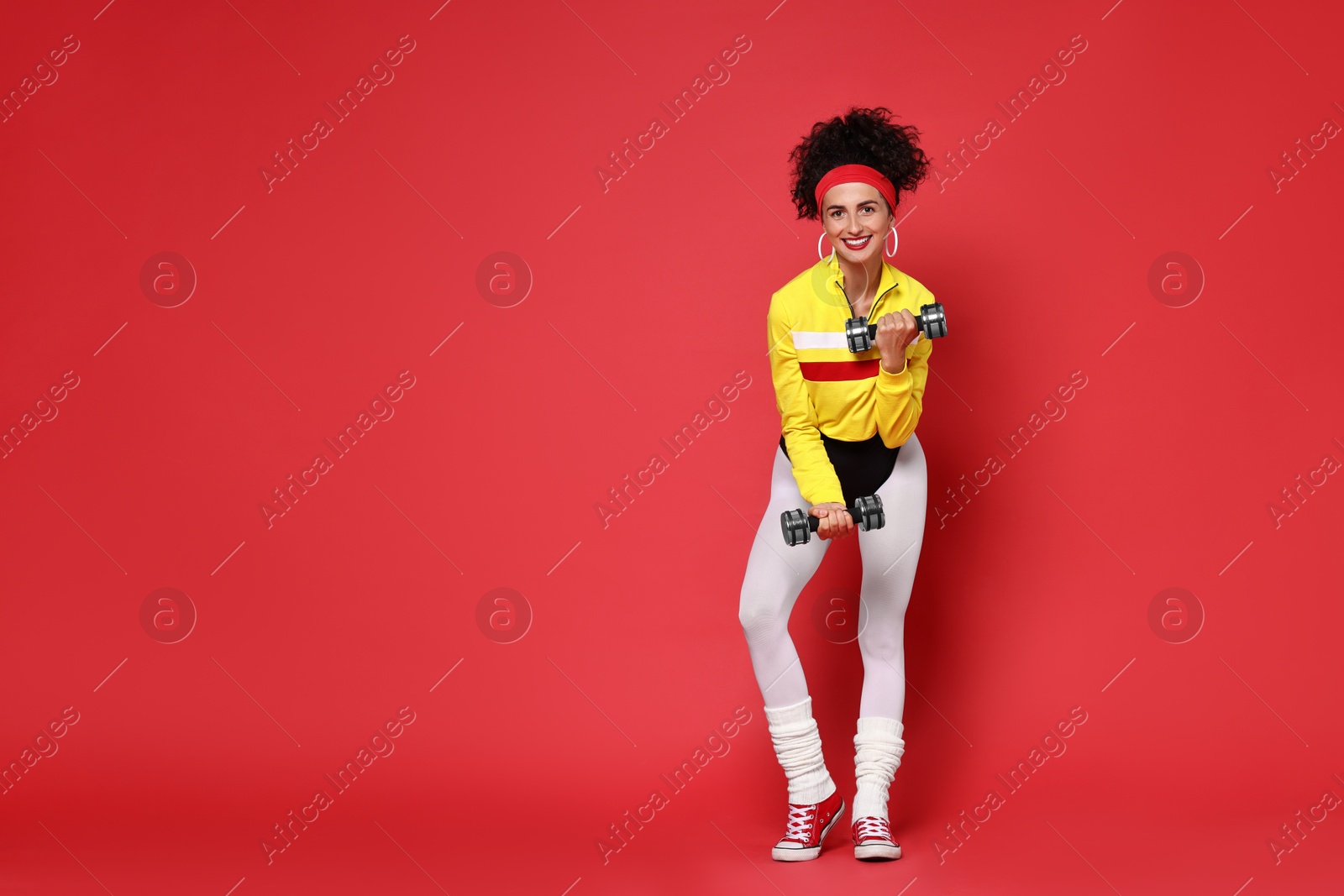 Photo of Woman doing aerobic exercise with dumbbells on red background