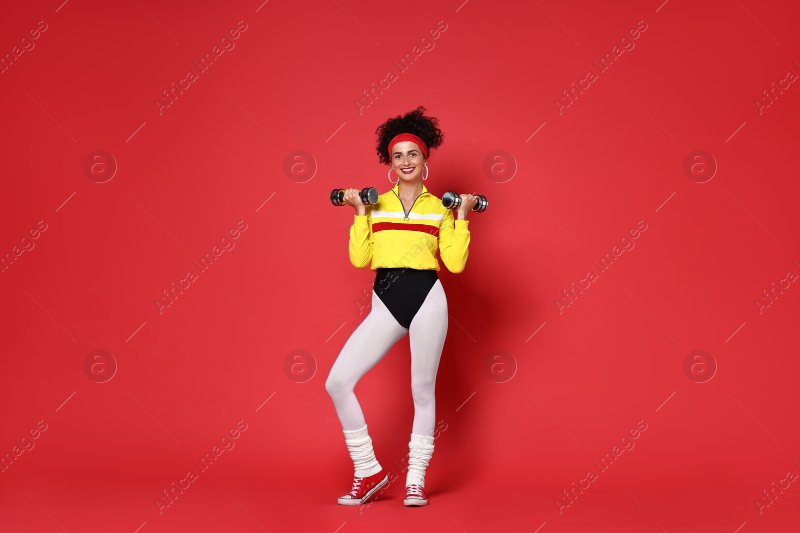 Photo of Woman doing aerobic exercise with dumbbells on red background