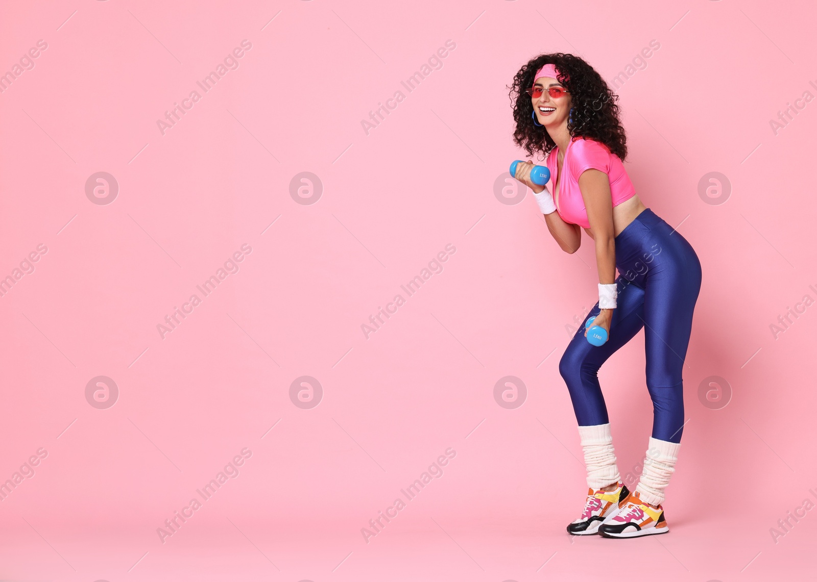 Photo of Woman doing aerobic exercise with dumbbells on pink background, space for text