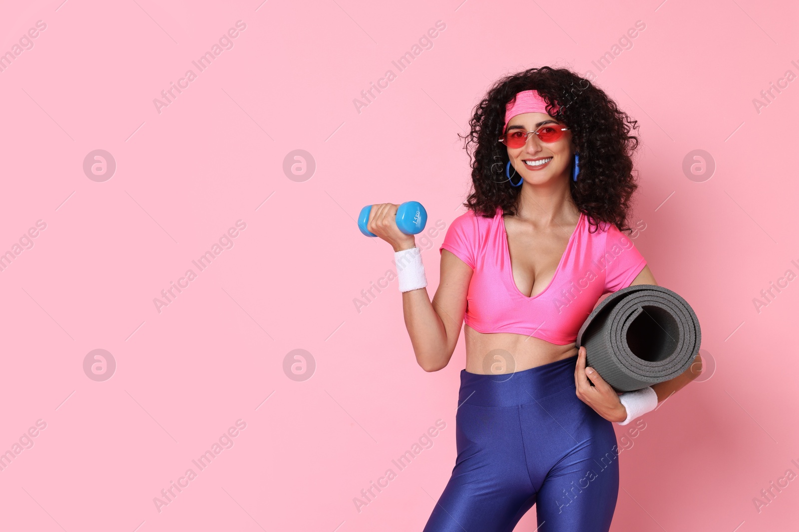 Photo of Aerobics. Happy woman with dumbbell and fitness mat on pink background, space for text