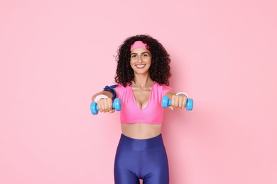 Photo of Woman doing aerobic exercise with dumbbells on pink background