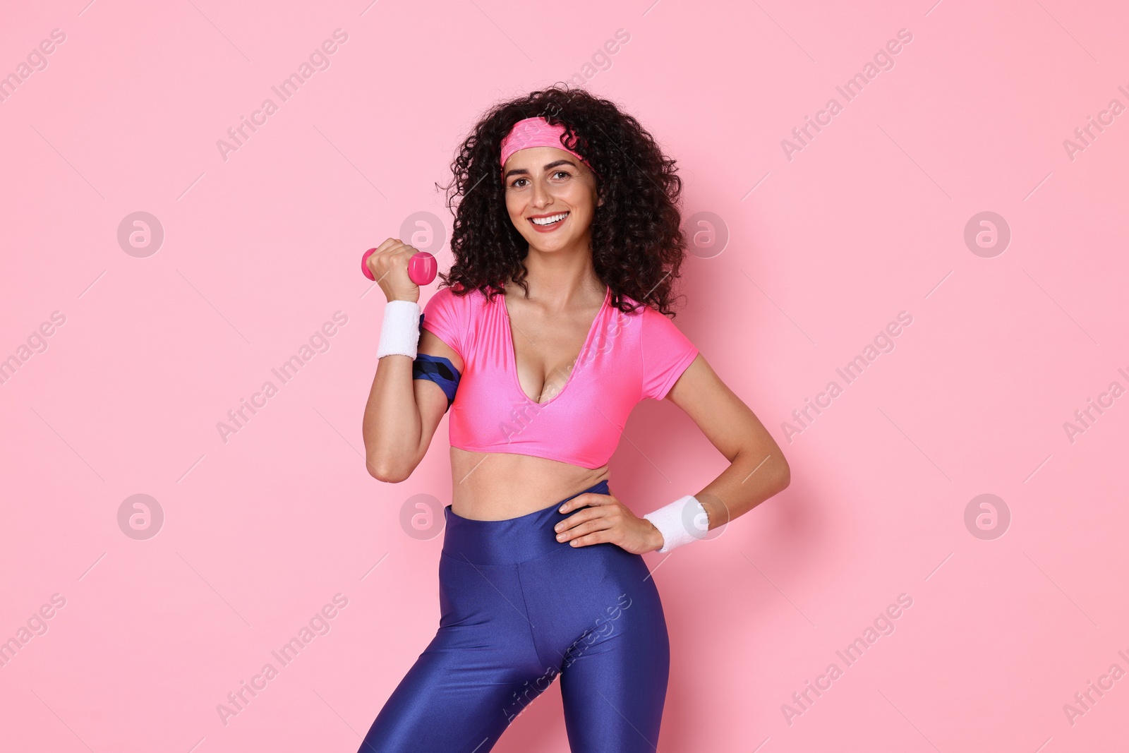 Photo of Woman doing aerobic exercise with dumbbell on pink background