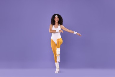 Happy woman doing aerobic exercise on purple background