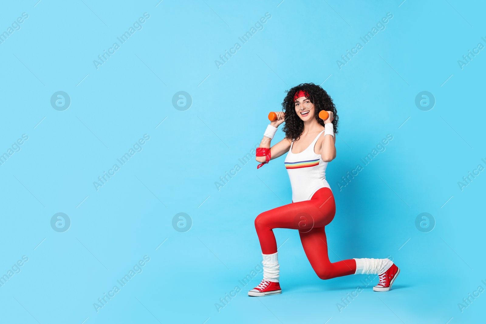 Photo of Woman doing aerobic exercise with dumbbells on light blue background, space for text