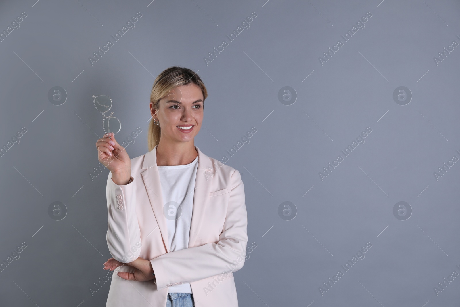 Photo of Beautiful woman in stylish jacket holding glasses on grey background, space for text