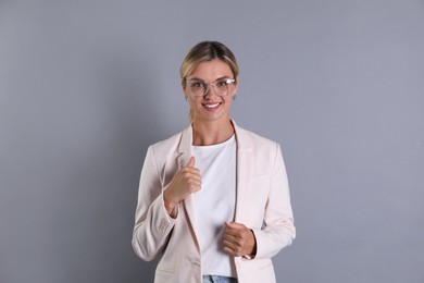 Beautiful woman in stylish jacket and glasses on grey background