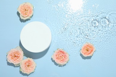 Photo of Beautiful rose flowers and round shaped podium in water on light blue background, flat lay. Space for text